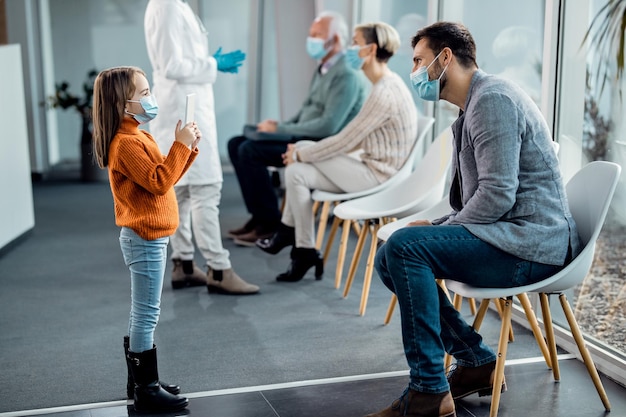 Small girl taking picture of her father with touchpad at hospital waiting room