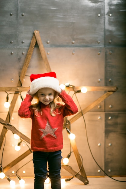 Free photo small girl with gifts on christmas sitting on red blanket by the star