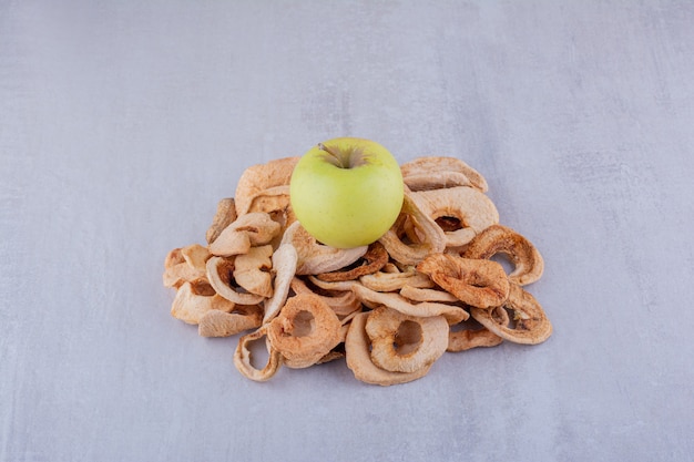 Free photo small heap of dried apple slices with a whole apple sitting on top on white background.