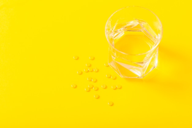 Small medicine tablets and glass of water over the yellow background