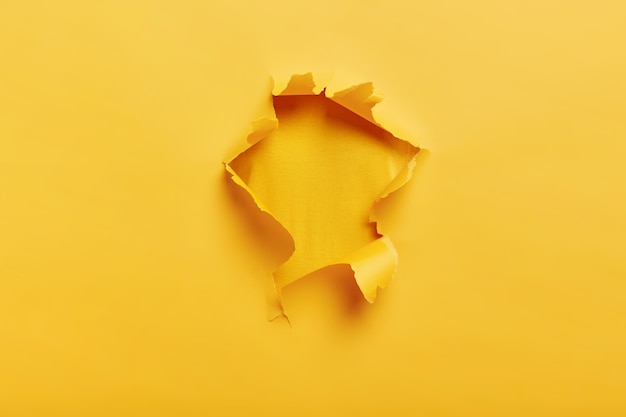 Free photo small paper hole with torn sides over yellow space for your text