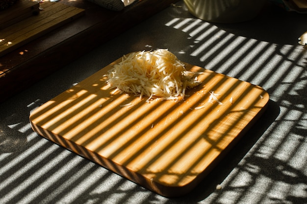 Free photo a small pile of grated fresh cheese lies on a wooden board in the kitchen