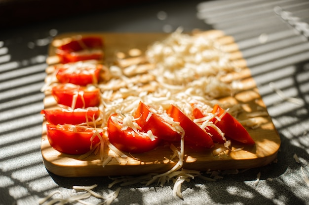 Free photo a small pile of grated fresh cheese and red tomatoes lies on a wooden board in the kitchen