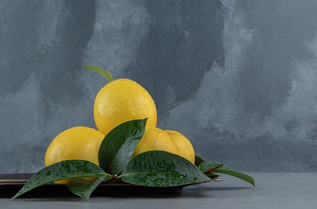 Free Photo small pile of lemons and leaves on an ornate tray on marble 