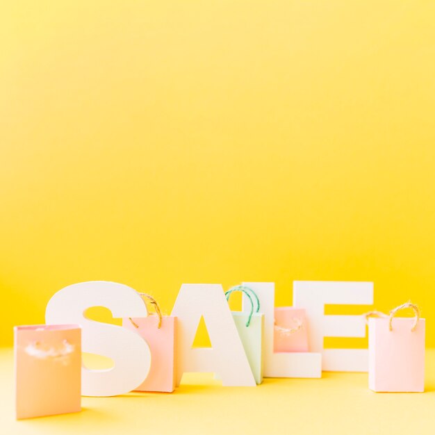 Free Photo small pink shopping bag in front of letter sale on yellow background