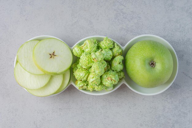 A small platter of apples and popcorn candyon marble surface