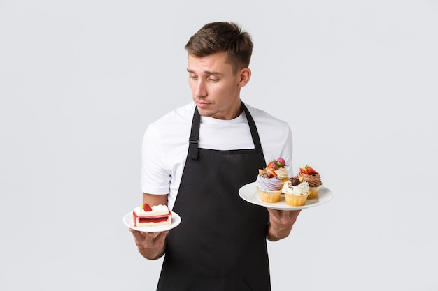 Free photo small retail business coffee shops and bakery concept handsome waiter in black apron looking at plat...