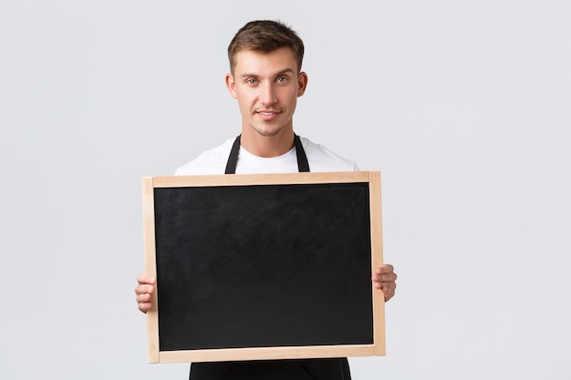 Small retail business owners, cafe and restaurant employees concept. Friendly good-looking salesman announce something to clients, holding board without signs, smiling happy, white background