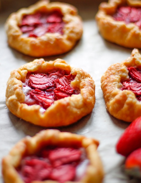 Free photo small rustic strawberry galette pie tarts with powdering sugar on oven tray