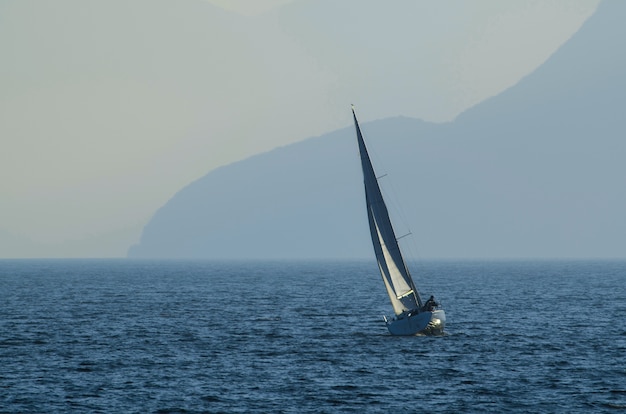 Free Photo small sailing ship on the sea surrounded by mountains covered in the fog at daytime