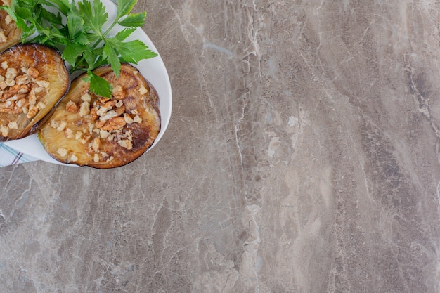 Small serving of fried indian eggplant slices garnished with chopped garlic and parsley, on marble.