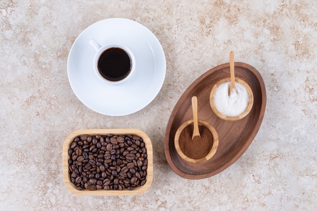 Free photo a small tray with bowls of sugar and ground coffee powder next to a cup of coffee and a bowl of coffee beans