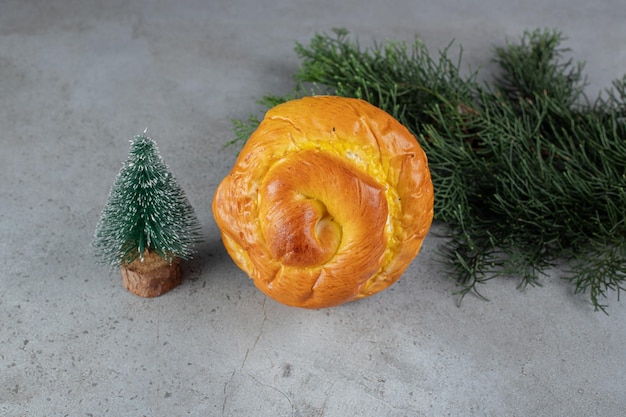 Small tree figurine, sweet bun and pine branch arranged on marble table.