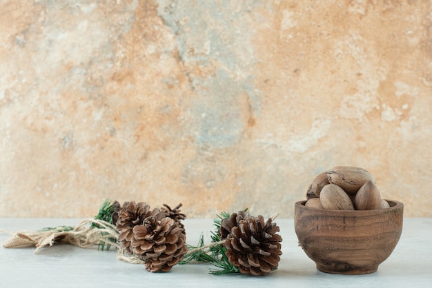 Free photo a small wooden bowl of nuts with pinecones on white background. high quality photo