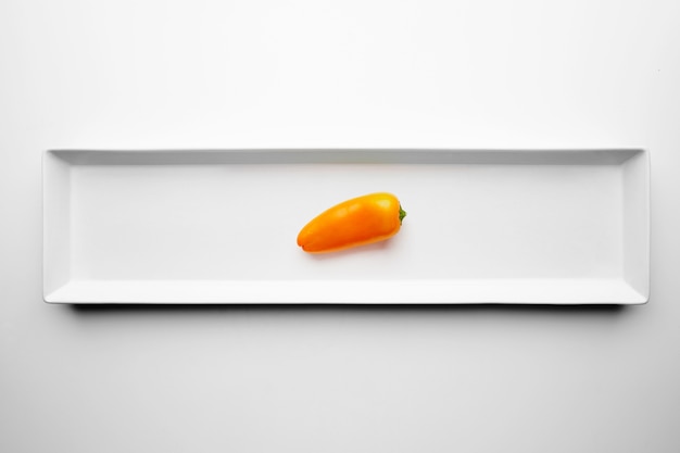 Small yellow pepper isolated in center ceramic rectangulat plate on white background table