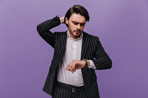 Smart attractive man with brunette hair, white shirt and trendy striped suit, looking at watch on his hand