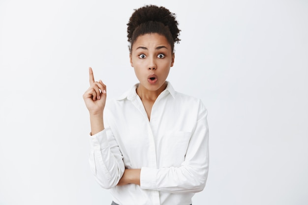 Smart, creative african-american lady entrepreneur in white-collar shirt, raising index finger in eureka gesture, folding lips, adding great suggestion during team meeting in office, having discussion