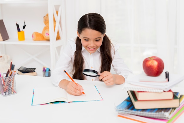 Smart Hispanic schoolgirl reading through magnifier