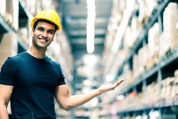 Smart Indian engineer man wearing safety helmet doing stock tick check and cardboard stock product management in factory warehouse background