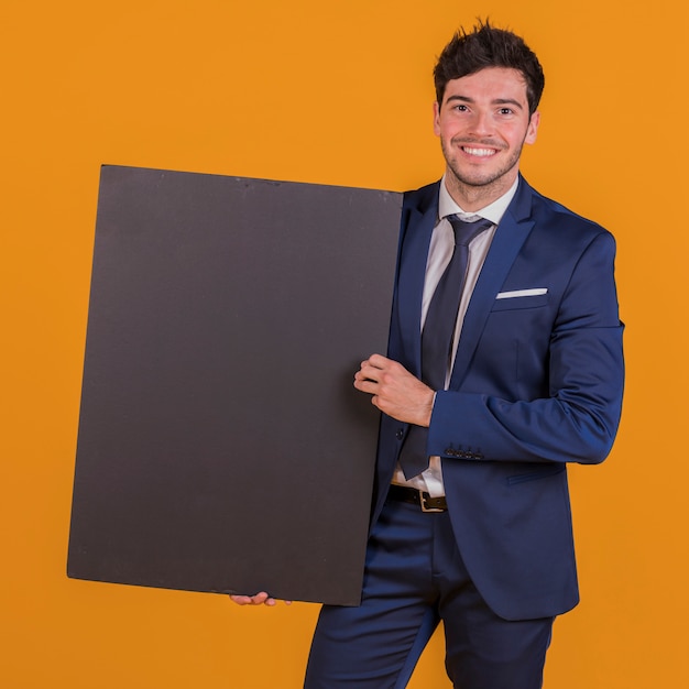 Free photo smart smiling young man holding black placard in hand against an orange backdrop