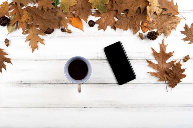 Smartphone and coffee cup on wooden leaves background