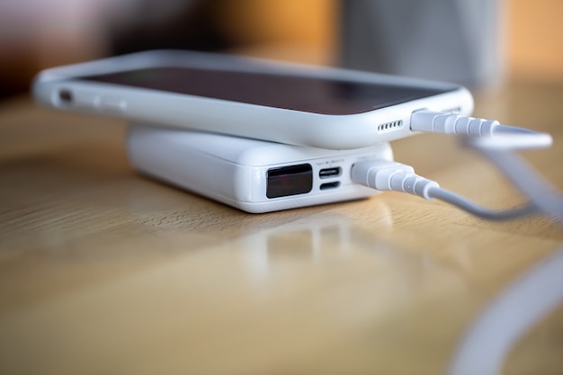 The smartphone is charged from a small white power bank via a cord, close up.