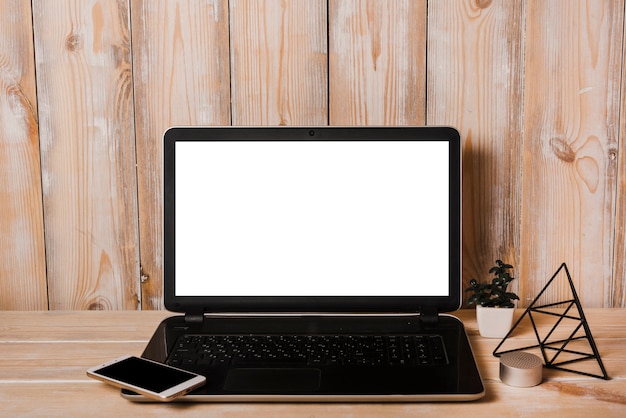 Smartphone on laptop with blank white screen on wooden desk