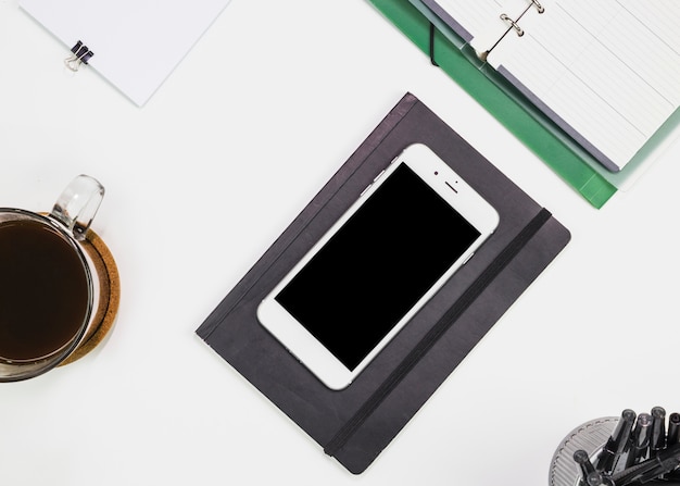 Smartphone near notebook and cup of drink