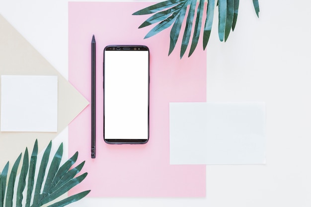 Free Photo smartphone near papers and palm trees on white desk