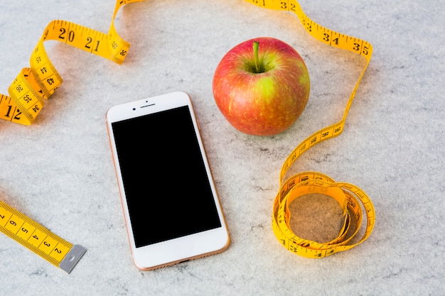 Free photo smartphone and red ripe apple with yellow measuring tape on gray textured background