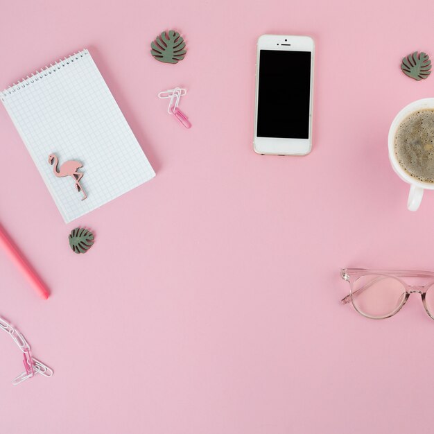 Smartphone with coffee cup and notepad on pink table