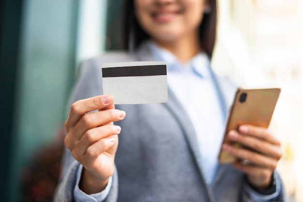 Smiley businesswoman with smartphone and credit card outdoors