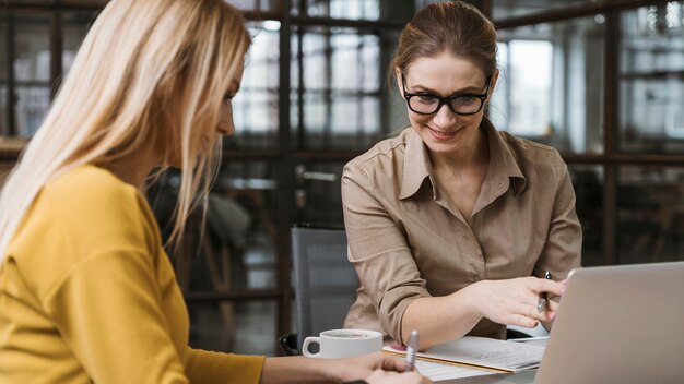 Smiley businesswomen working with laptop at desk indoors