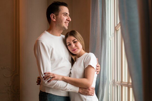 Smiley couple embraced next to window