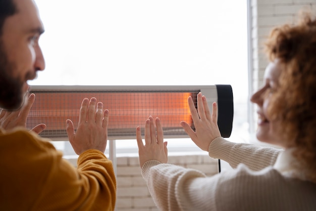 Free photo smiley couple warming up hands near heater