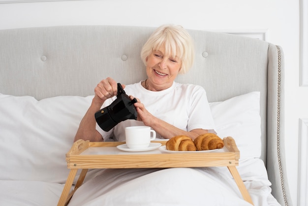 Smiley elder woman holding kettle in the bedroom