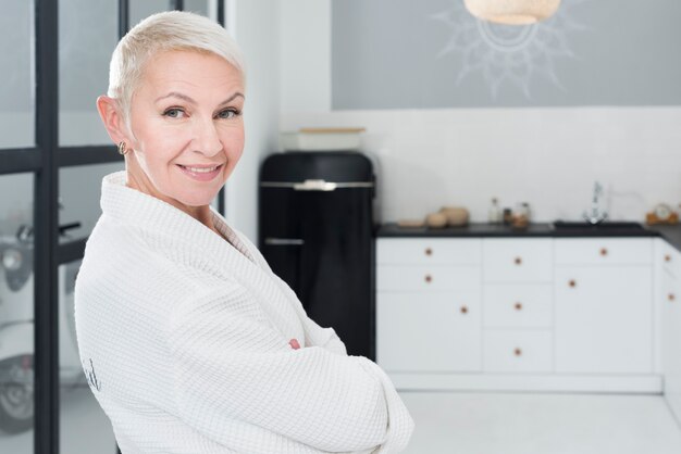 Smiley elder woman posing in bathrobe in the kitchen