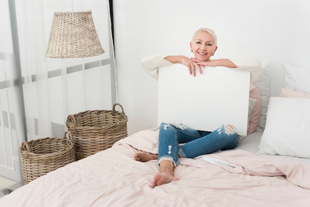 Smiley elderly woman holding blank placard in bed