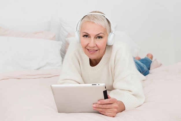 Smiley elderly woman holding tablet and listening to music on headphones