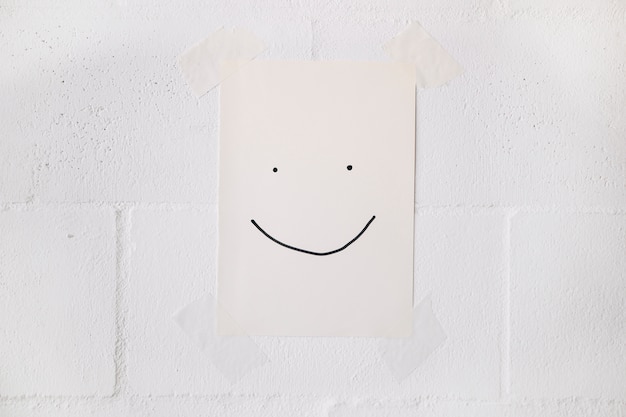 Free Photo smiley face made on white paper stick on wall with tape