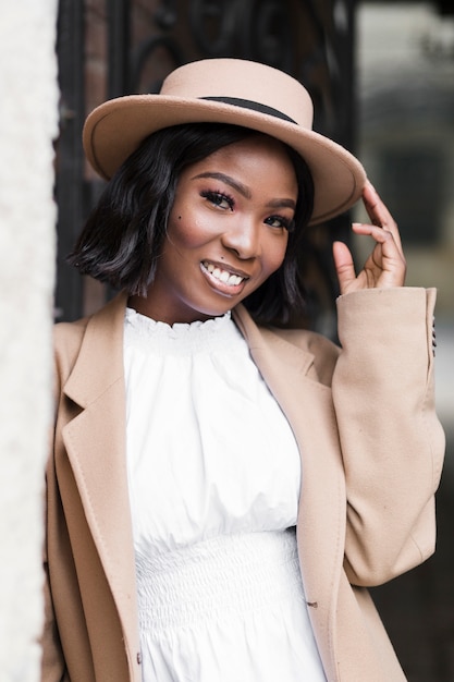 Smiley fashionable woman posing while holding her hat outside