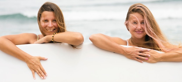 Smiley female friends at the beach with surfboard