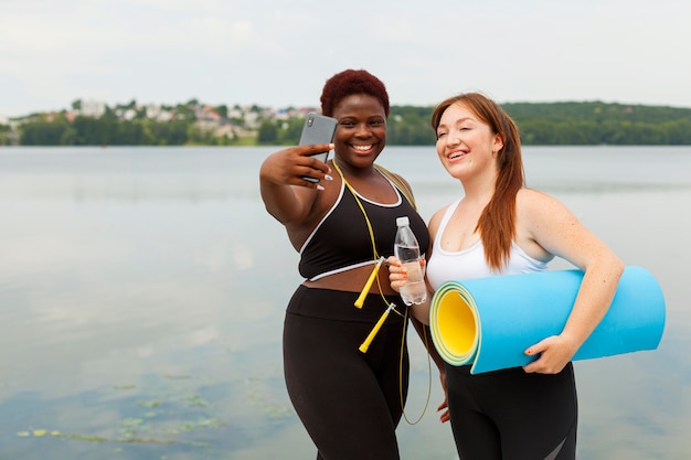 Smiley female friends taking selfie outdoors while exercising