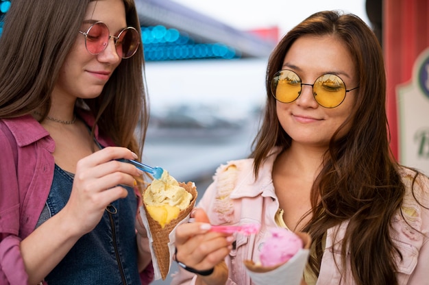 Free photo smiley female friends with sunglasses eating candy