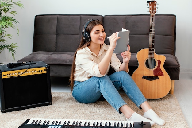 Smiley female musician writing songs on notepad next to acoustic guitar and keyboard