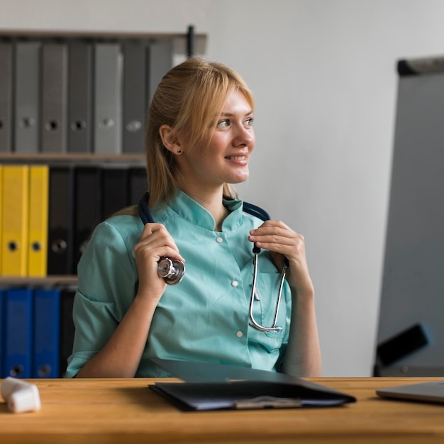 Free photo smiley female nurse in the office with laptop