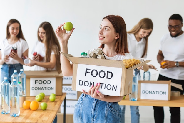 Free photo smiley female volunteer holding food donations box with apple