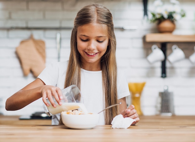 Smiley girl pouring milk in a cereal bowl