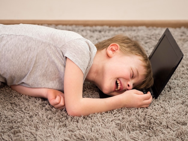 Free photo smiley kid laying with his head on a laptop