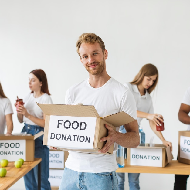 Free photo smiley male volunteer holding box of food donations